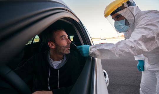 Lab tech in protective gear checks patient in car