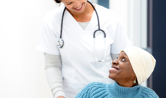 nurse in white scrubs pushing oncology patient wearing blue sweater in wheel chair